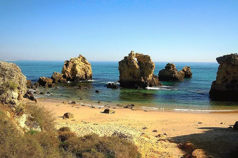 Pequenos ilhéus rochosos emergindo do mar na Praia dos Arrifes, Albufeira.