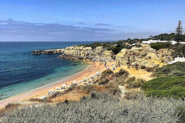 Areal dourado da Praia do Castelo enquadrado por penhascos esculpidos.