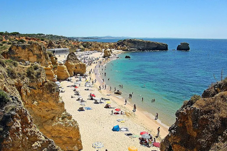 Areal dourado e águas cristalinas da Praia de São Rafael num dia de sol no Algarve.